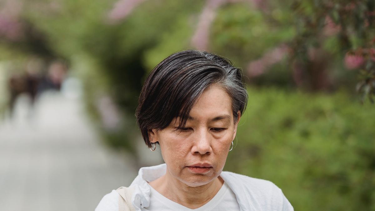 屋外で伏し目がちな中高年女性（更年期障害のイメージ）