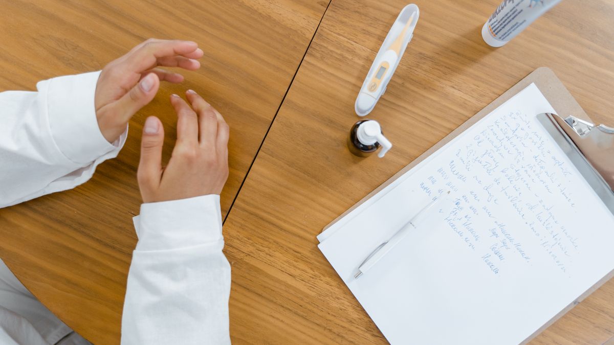 診察デスクの上のカルテと体温計、記録する医師の手元