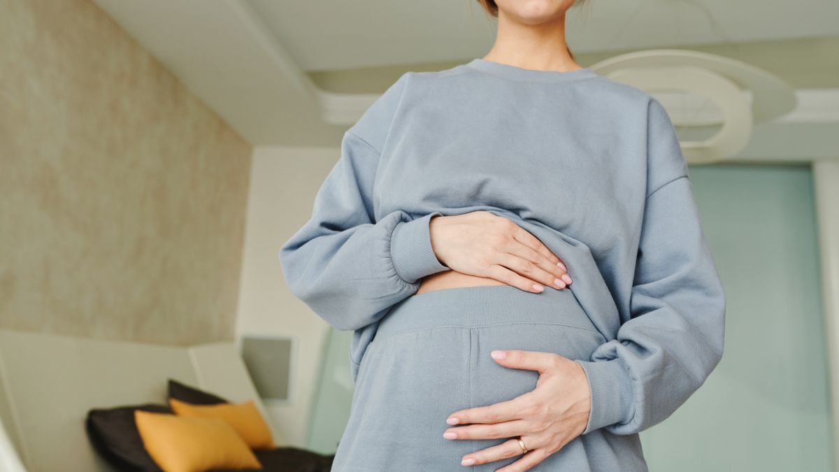 クリニックの一室で、両手でそっとおなかを支える妊婦