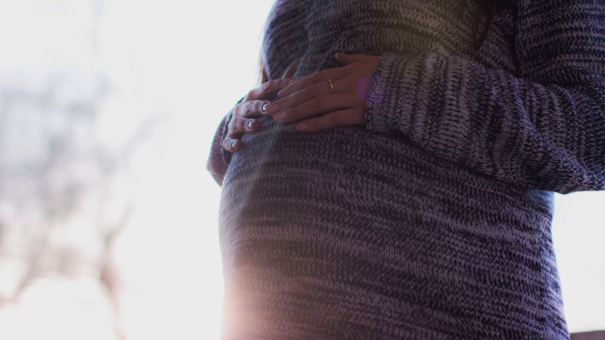 やわらかな光のなかで、おなかにそっと手をあてる妊婦