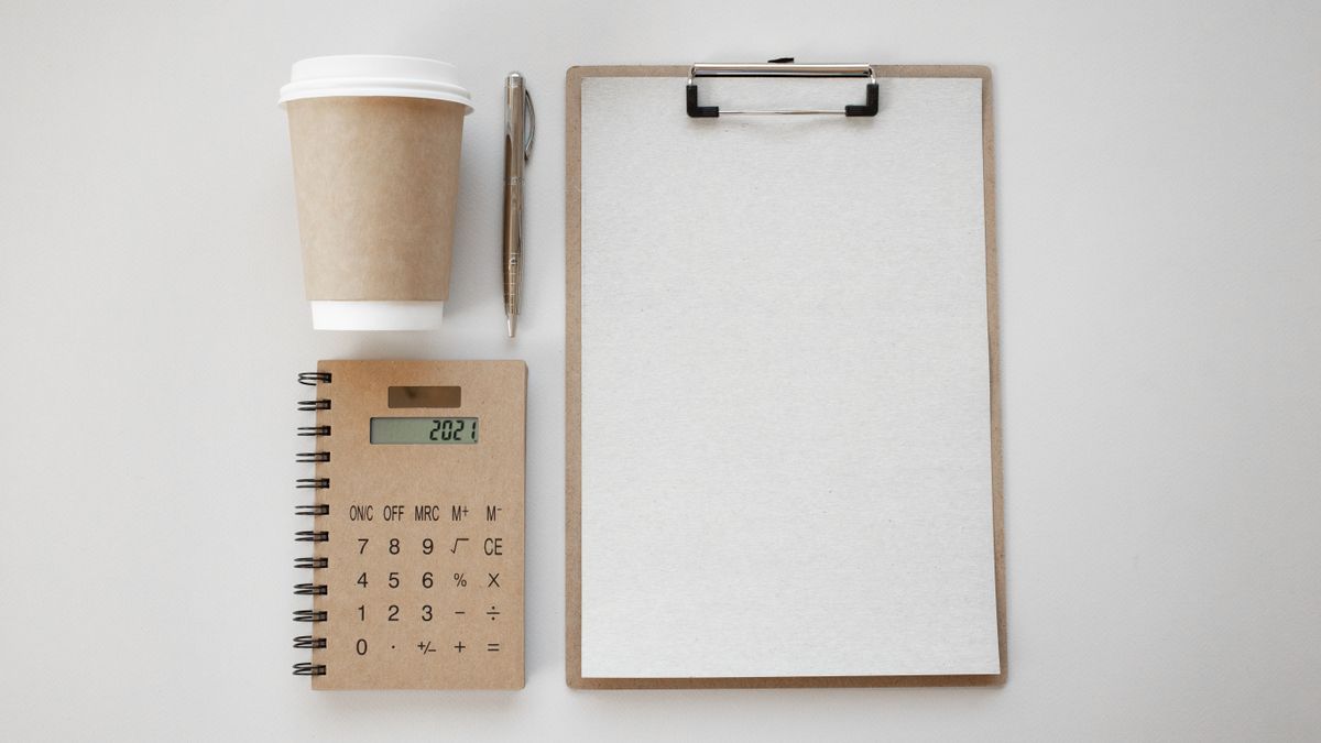 机の上に置かれた電卓とクリップボード、コーヒー。費用を確認するイメージ